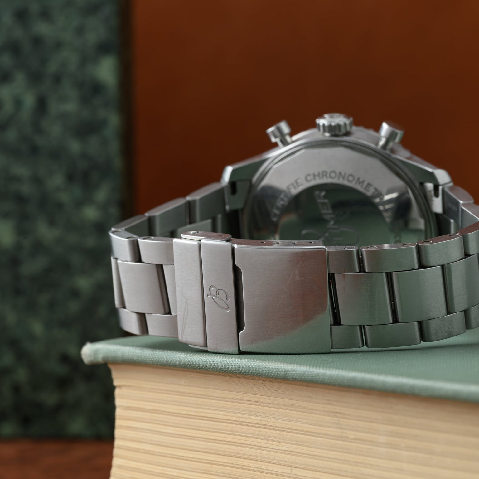 A Breitling Navitimer 8 Chronograph with a silver metal strap rests on a closed book, displaying its clasp and part of the watch back.