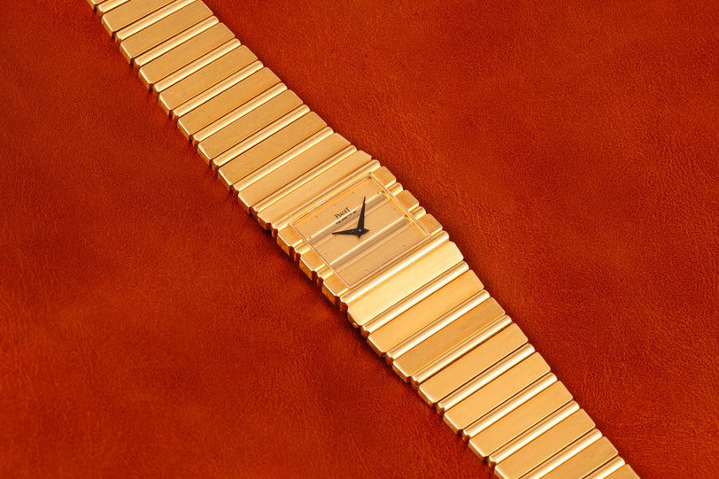 A Piaget Polo gold wristwatch with a square face rests on a brown leather surface.