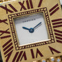 Gold-toned Cartier watch face with square dial, white center, blue hands, burgundy Roman numerals, and decorative beaded bord