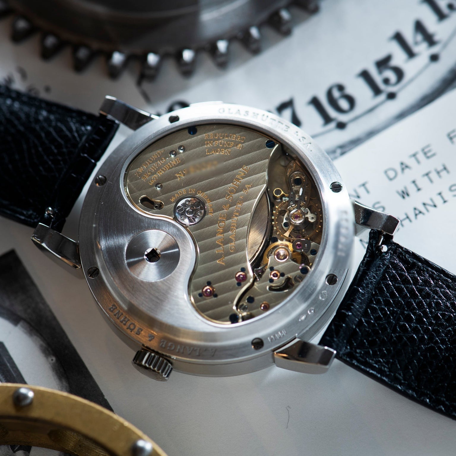 Close-up of the Lange & Sohne Lange 31s exposed mechanical movement, revealing intricate gears and engravings, with its black leather strap in view.