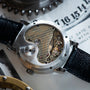 Close-up of the Lange & Sohne Lange 31s exposed mechanical movement, revealing intricate gears and engravings, with its black leather strap in view.