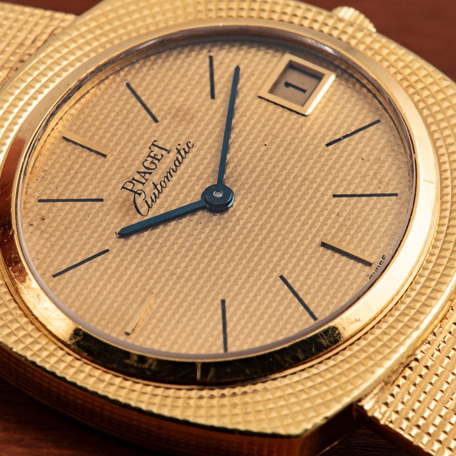 Piaget Yellow Gold Hobnail Dress Watch featuring blue hands, black hour markers, and a date window displaying 1 on the dial.