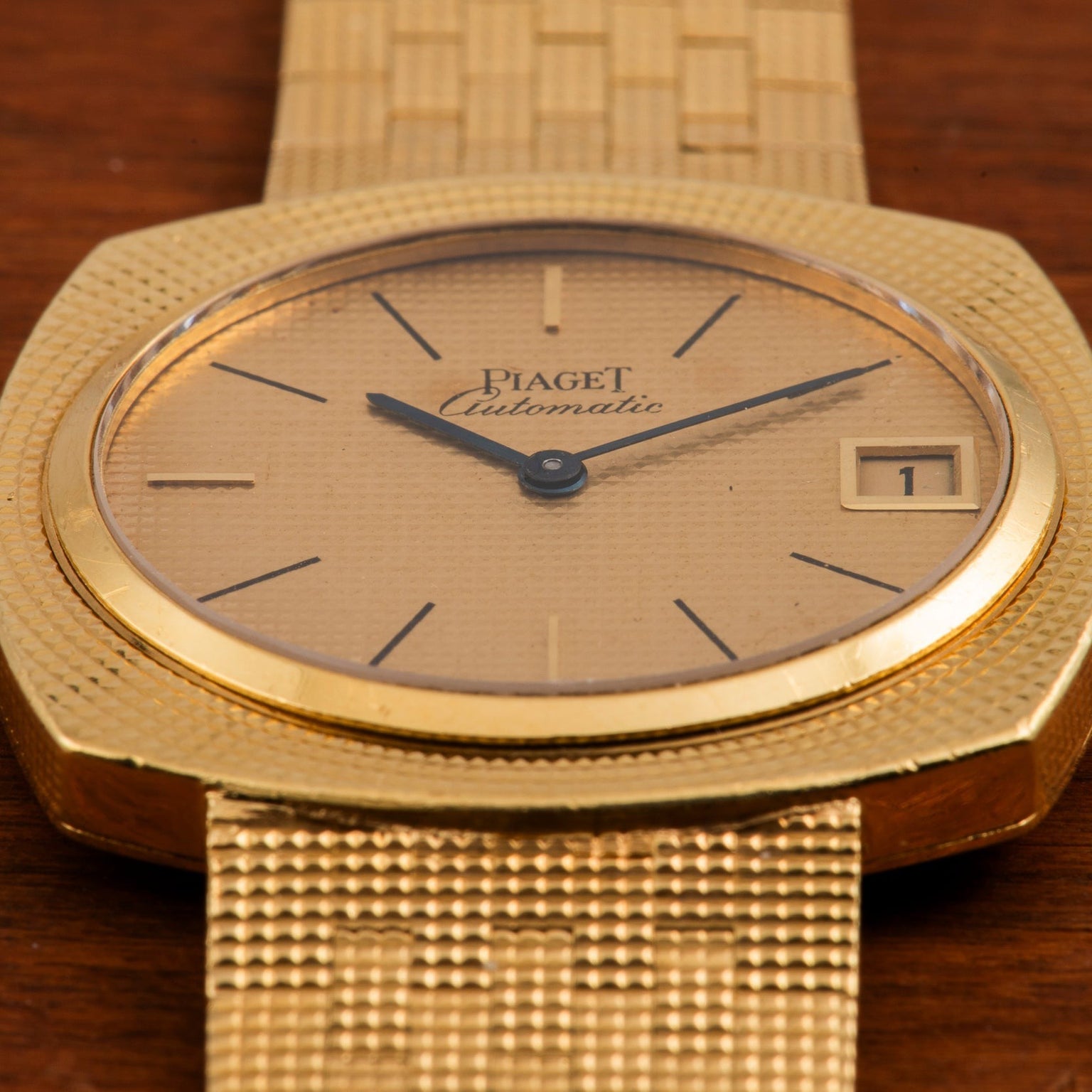 Piaget Yellow Gold Hobnail Dress Watch with a textured dial and date window, displayed on a wooden surface.