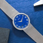 The Piaget Lapis Lazuli Dress Watch features a silver design with a blue face and Roman numerals, displayed on a textured blue surface.