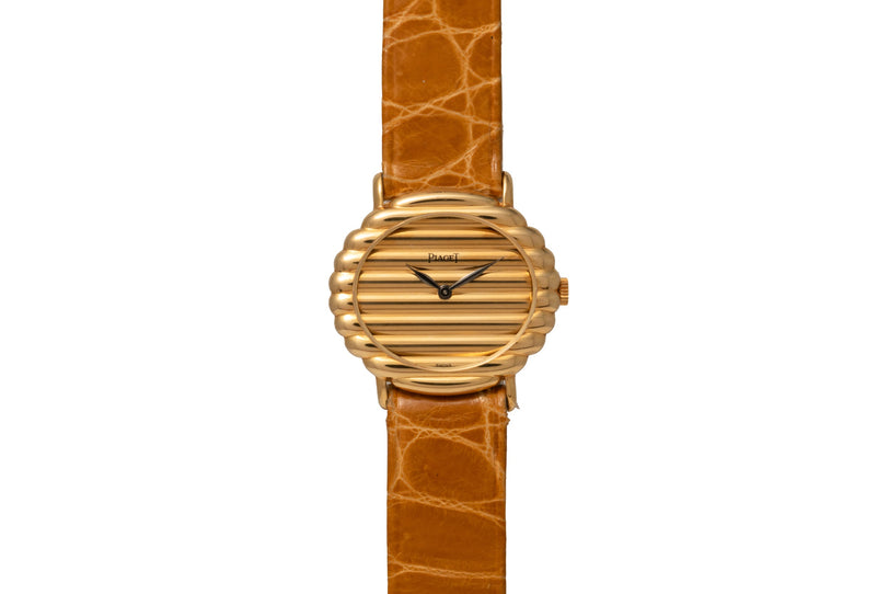 Piaget Ovale gold watch featuring a ridged circular face and brown leather strap, viewed from above on a white background.