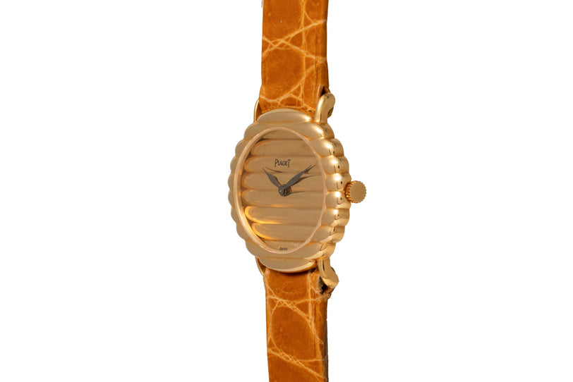 The Piaget Ovale wristwatch features a textured oval face, brown leather strap, and displays the time as 9:05.