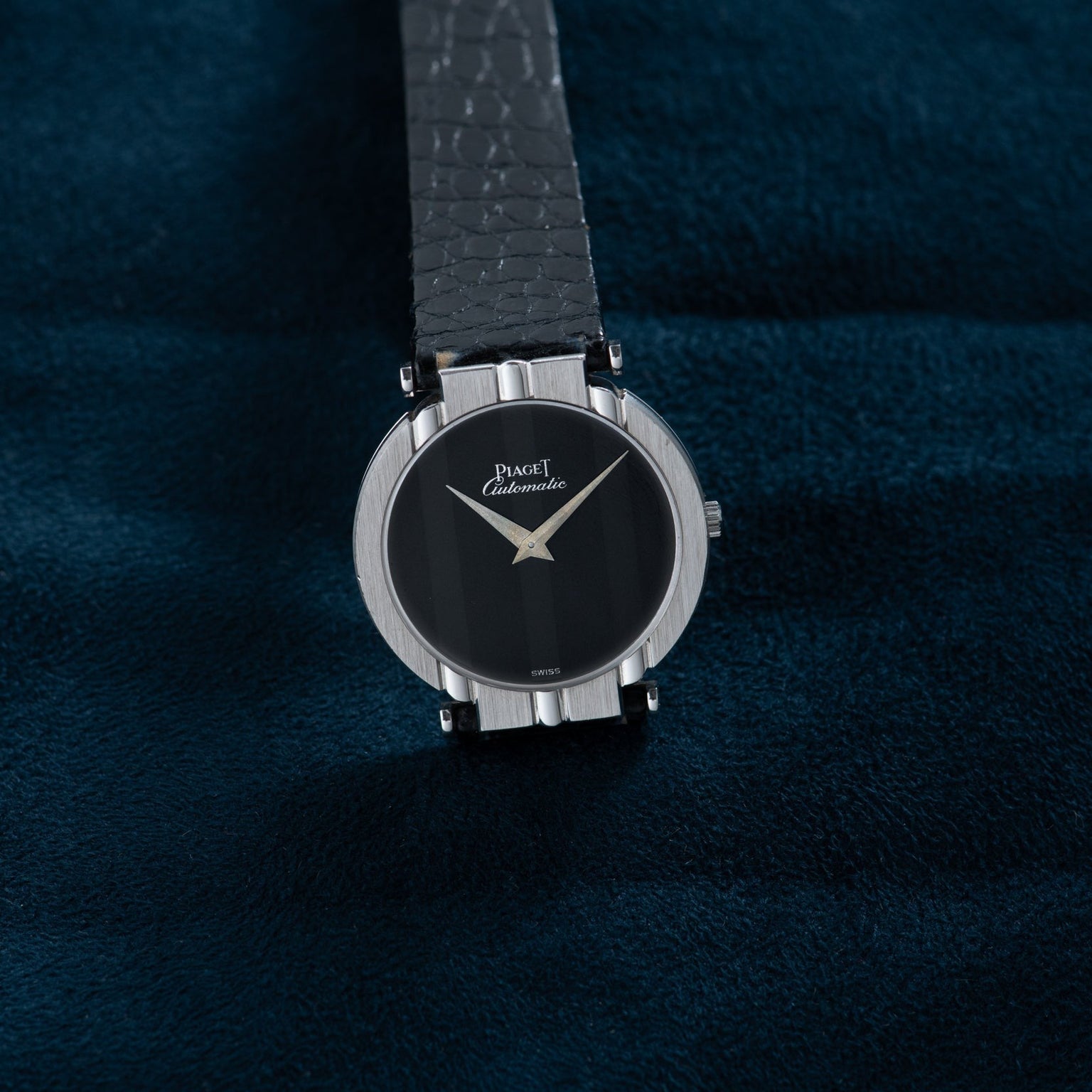 A Piaget White Gold Ladies wristwatch rests on a dark blue textured surface.
