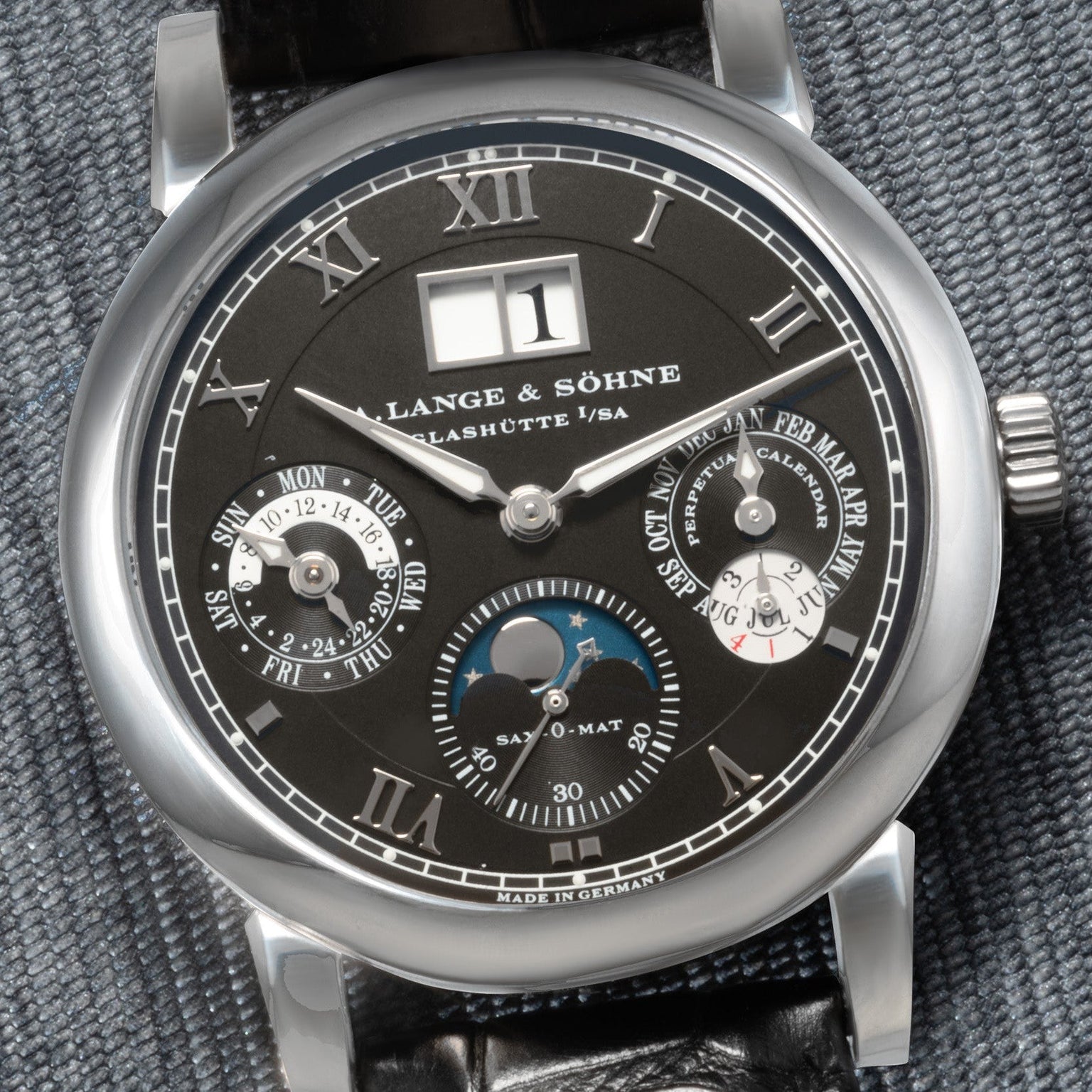 Close-up of a black Lange & Sohne Langematik Perpetual Calendar wristwatch with Roman numerals and multiple subdials on a textured surface.