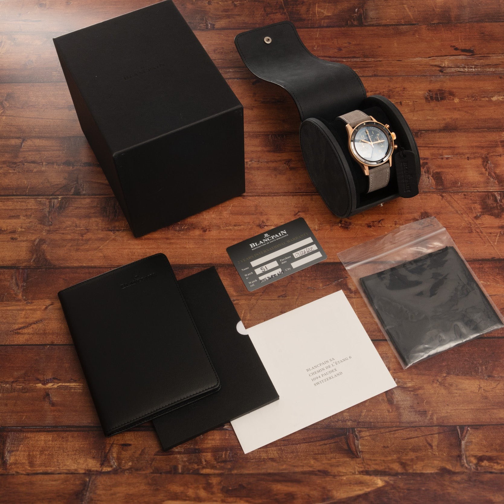 The Blancpain Air Command Flyback Chronograph luxury watch is displayed with its box, case, card, cloth, and booklet arranged on a wooden surface.