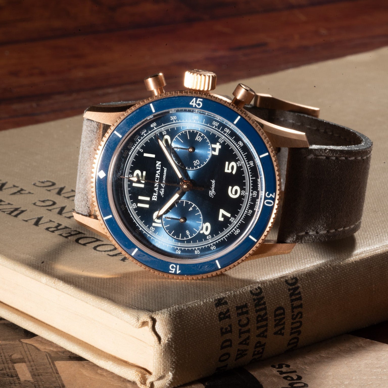 The Blancpain Air Command Flyback Chronograph, featuring a blue face and brown leather strap, rests atop a closed vintage book.