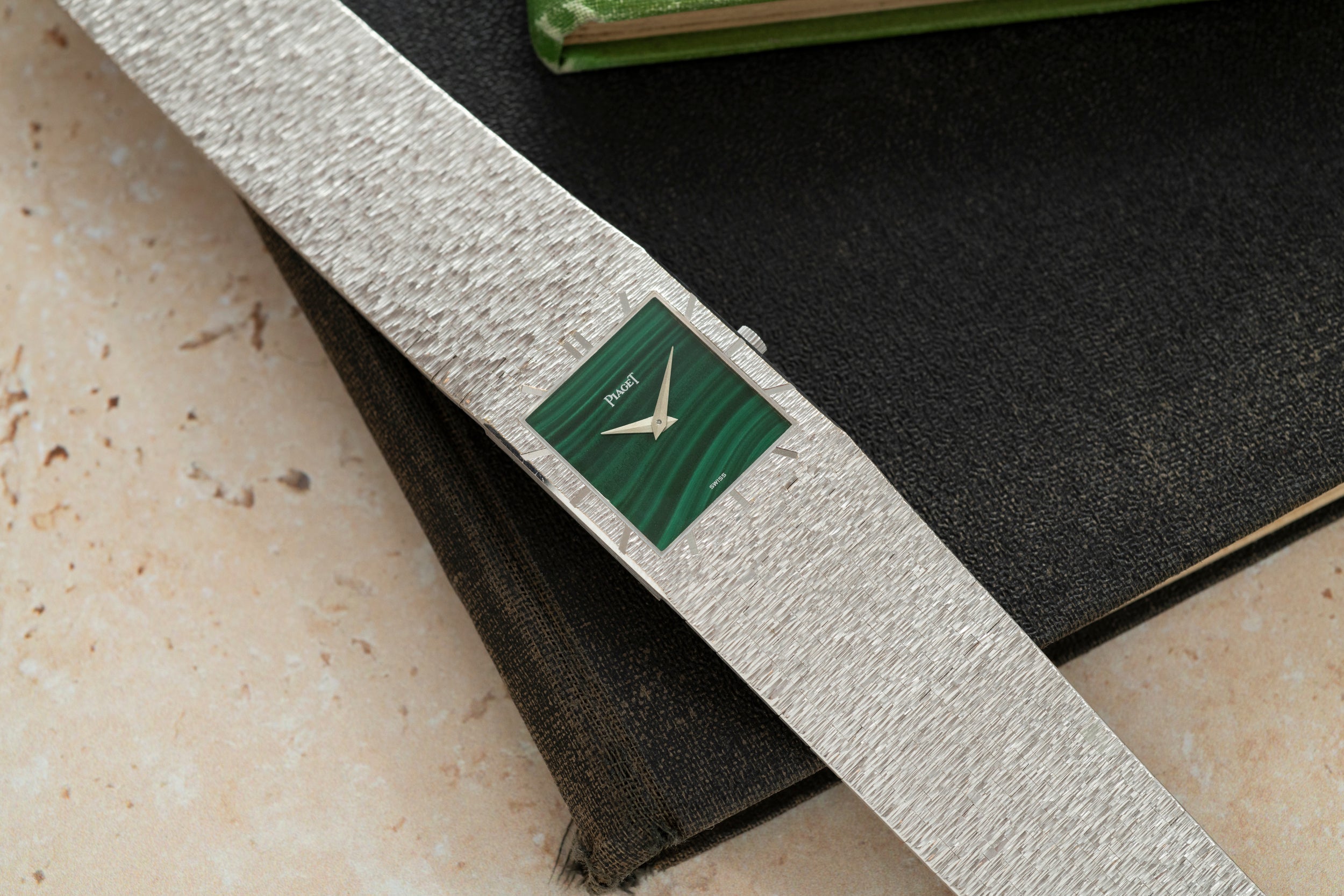 A Piaget White Gold Malachite Dress Watch with a green square face rests atop two closed books.