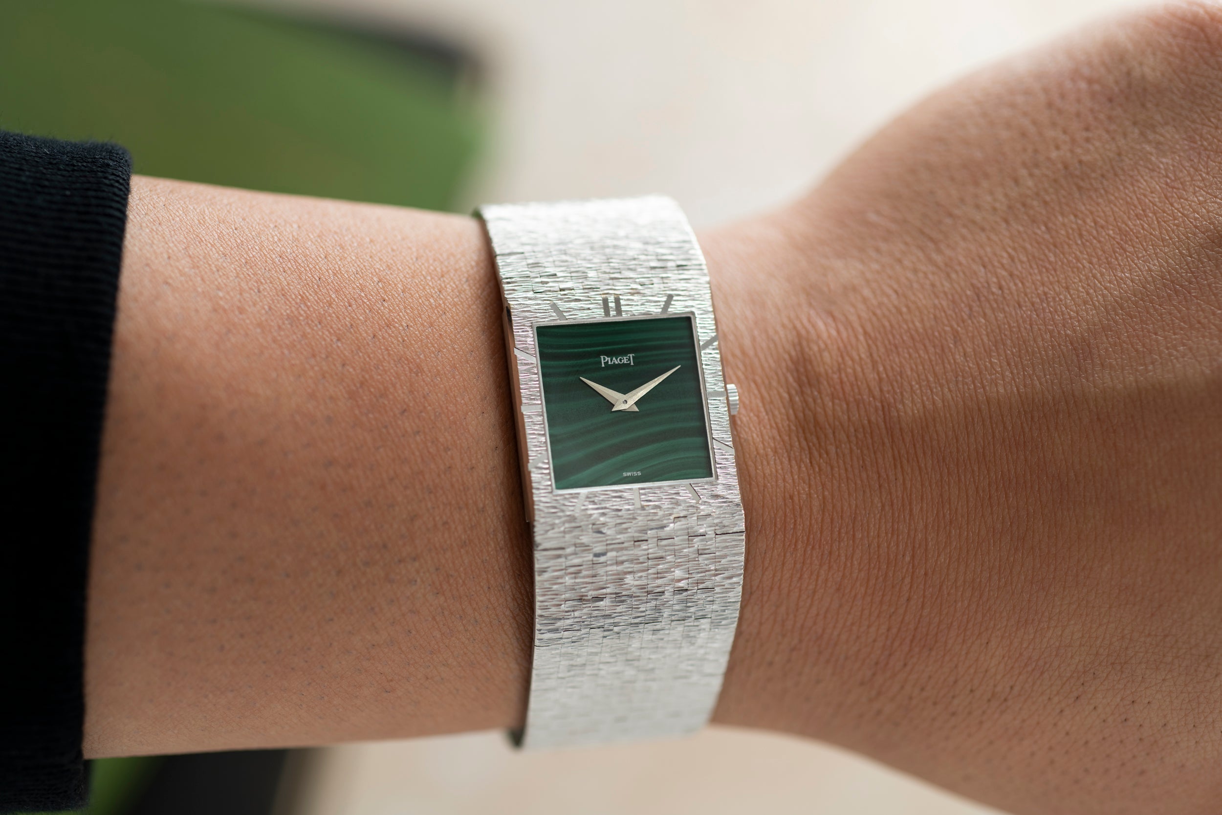 A Piaget White Gold Malachite Dress Watch with a green square face is worn on a person’s wrist.