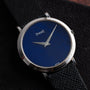 A Piaget Ladies Lapis Lazuli Dress Watch with a blue dial and black textured leather strap rests on a dark surface.