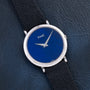 A Piaget Ladies Lapis Lazuli Dress Watch with a blue face and black leather strap is displayed on a textured dark surface.