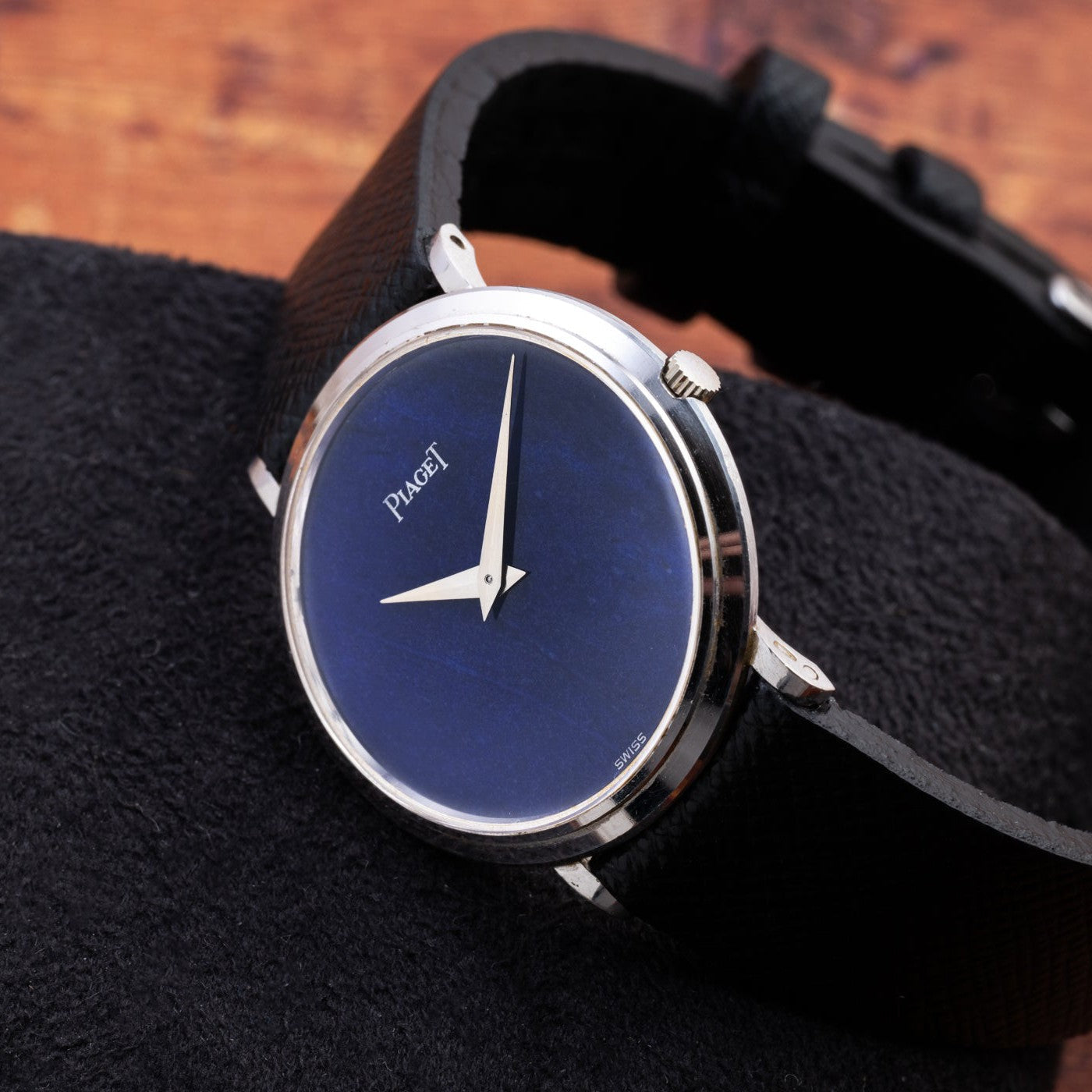 The Piaget Ladies Lapis Lazuli Dress Watch, featuring a striking blue face and black leather strap, is displayed on a dark textured surface.