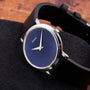 The Piaget Ladies Lapis Lazuli Dress Watch, featuring a striking blue face and black leather strap, is displayed on a dark textured surface.