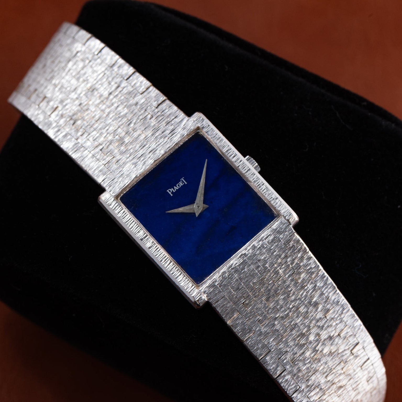 A Piaget white gold Lapis Lazuli dress watch with a blue rectangular face is displayed on a black cushion.