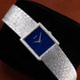 A Piaget white gold Lapis Lazuli dress watch with a blue rectangular face is displayed on a black cushion.