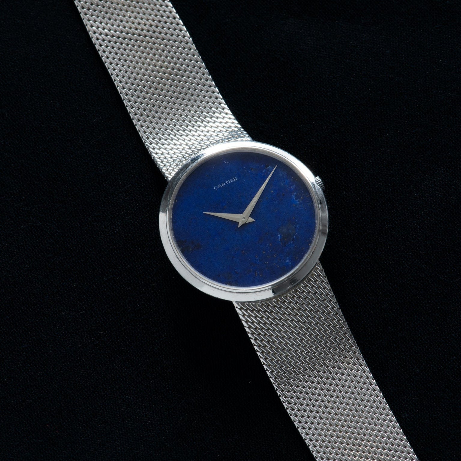 A White Gold Lapis by Piaget wristwatch from Cartier featuring a blue face and silver hands, set against a black background.