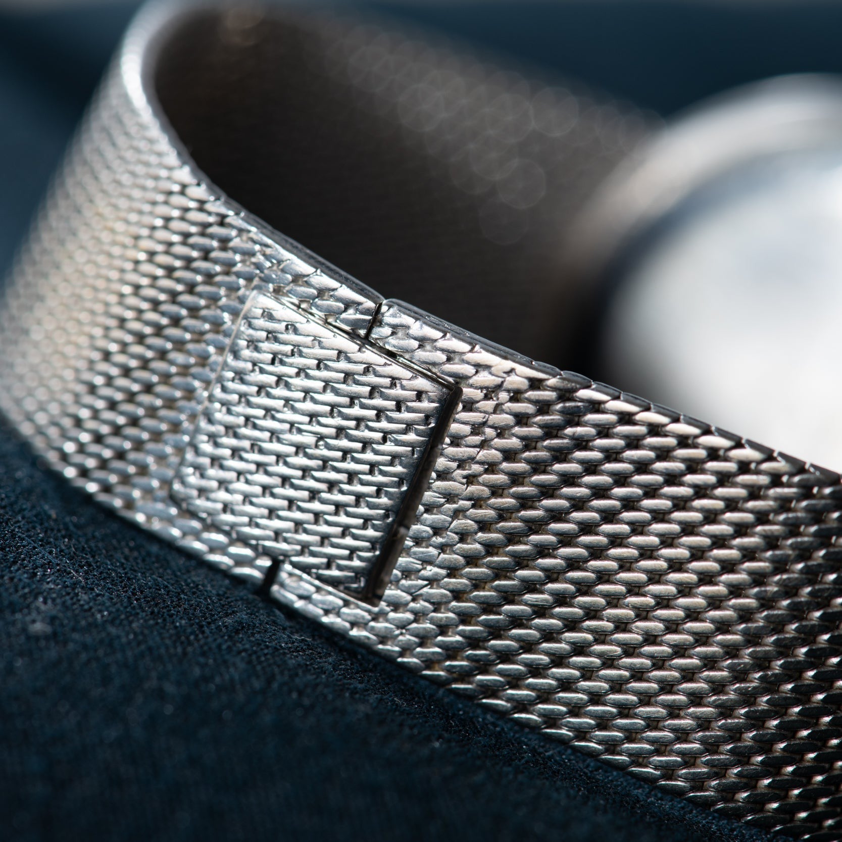 Close-up of the White Gold Lapis by Piaget, a Cartier watch featuring a silver mesh metal band with clasp, set against a dark background.