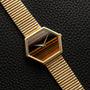The Piaget Hexagonal Tigers Eye wristwatch features a gold case and a striped brown dial, displayed on a textured black surface.