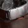 Close-up of an OMEGA Seamaster 300 Professional Apnea Chronograph stainless steel clasp resting on a brown leather surface.