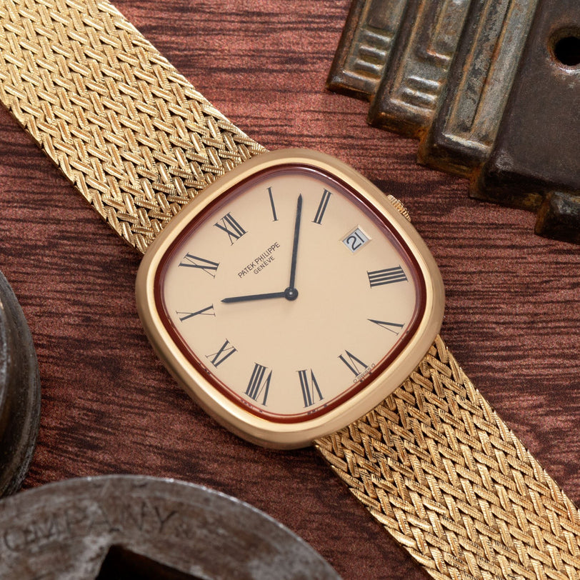 Patek Philippe Ellipse TV Case watch with Roman numerals and a woven strap, displayed on a wooden surface.