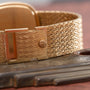 A close-up of the gold textured clasp of a Patek Philippe Ellipse TV Case watch band resting on a wooden surface.