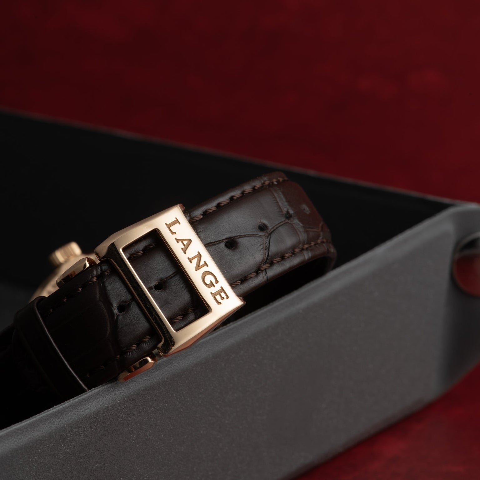 Close-up of a brown leather strap with a gold buckle engraved LANGE, part of the Lange & Sohne Lange 1 Tourbillon, displayed on a dark tray.