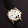 The Lange & Söhne Lange 1 Tourbillon features a gold case, leather strap, and visible tourbillon, elegantly displayed on a dark surface.