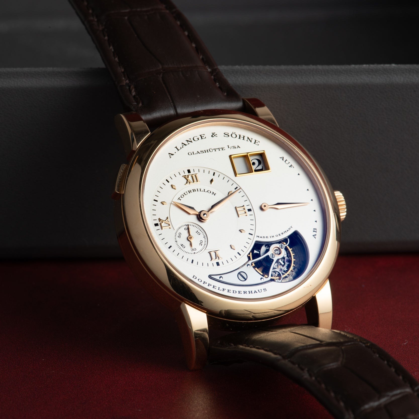 The Lange & Sohne Lange 1 Tourbillon is a luxury wristwatch featuring a white dial, gold case, and brown leather strap.