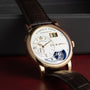 The Lange & Sohne Lange 1 Tourbillon is a luxury wristwatch featuring a white dial, gold case, and brown leather strap.
