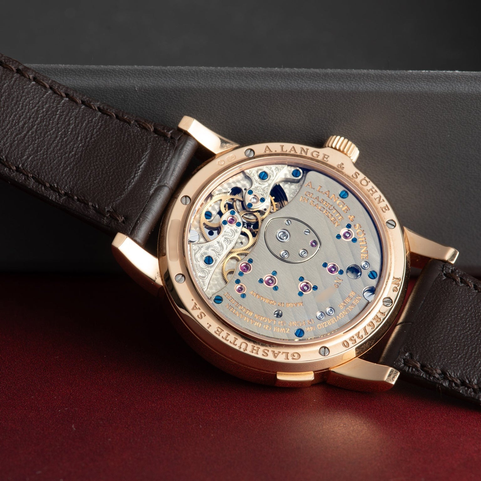 The Lange & Sohne Lange 1 Tourbillon is a luxury watch with an open case back revealing intricate mechanical movement and features a brown leather strap.