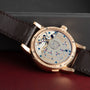 The Lange & Sohne Lange 1 Tourbillon is a luxury watch with an open case back revealing intricate mechanical movement and features a brown leather strap.