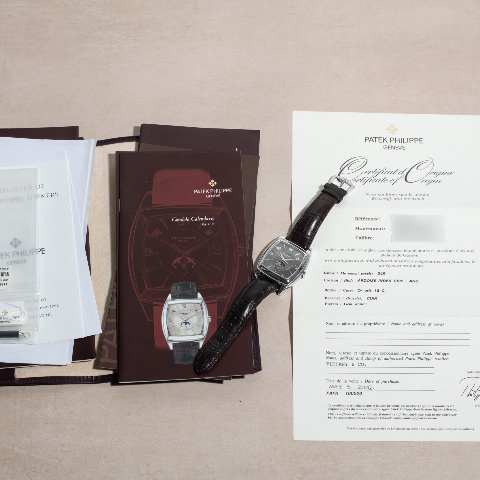A Patek Philippe Gondolo Annual Calendar watch displayed on a beige surface with its certificate, manuals, and documents.