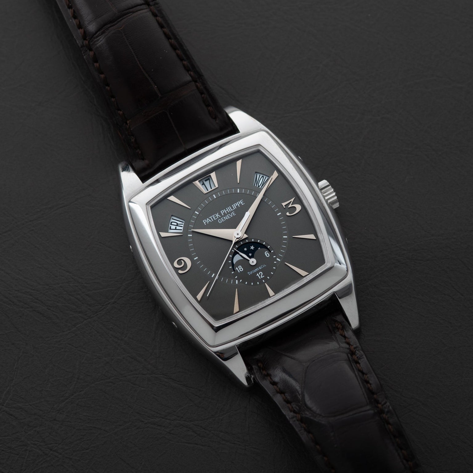 The Patek Philippe Gondolo Annual Calendar features a square black dial and a black leather strap, elegantly displayed on a dark surface.