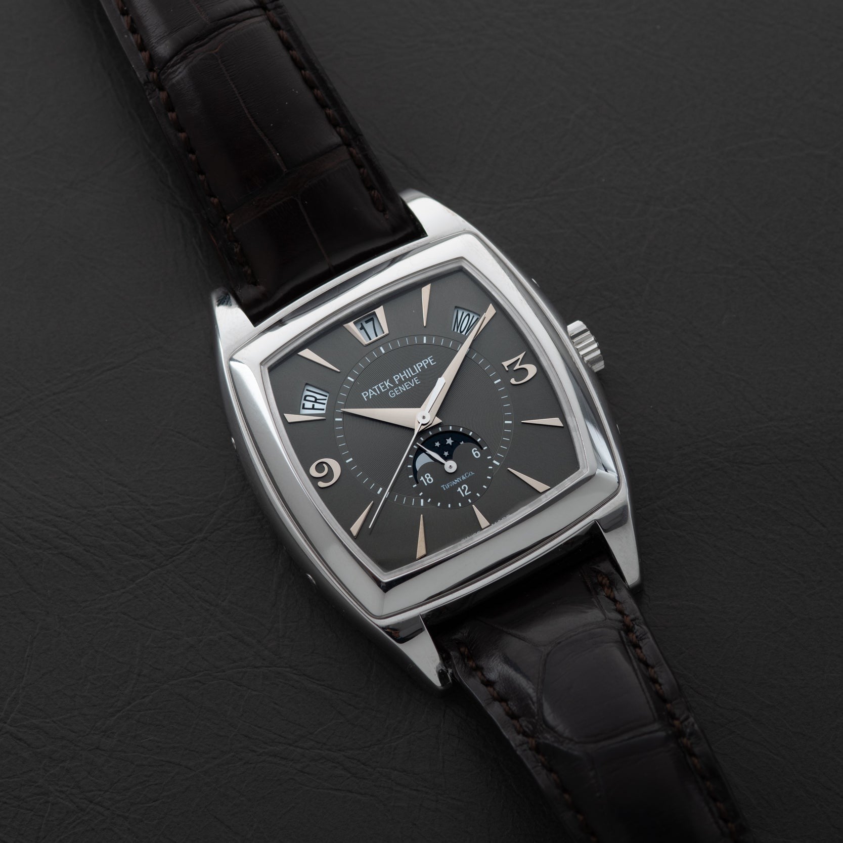 The Patek Philippe Gondolo Annual Calendar features a square black dial and a black leather strap, elegantly displayed on a dark surface.