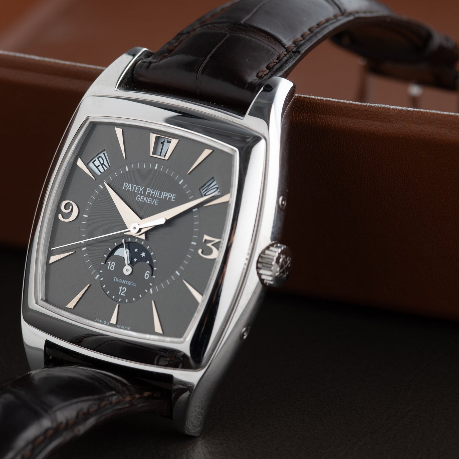 A Patek Philippe Gondolo Annual Calendar wristwatch featuring a rectangular silver case and brown leather strap, displayed on a leather surface.
