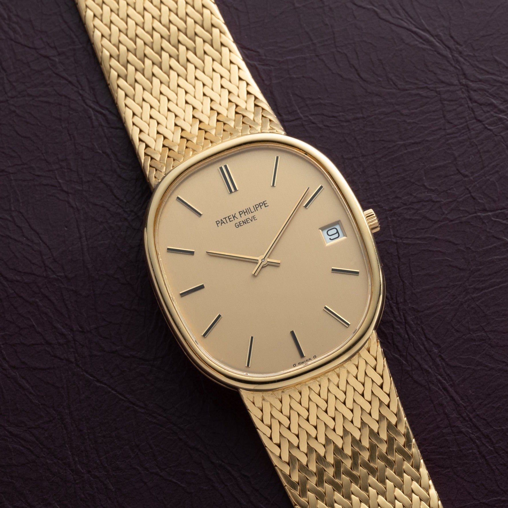 Patek Philippe Ellipse Jumbo watch with woven bracelet, beige dial, and date display on a dark textured surface.