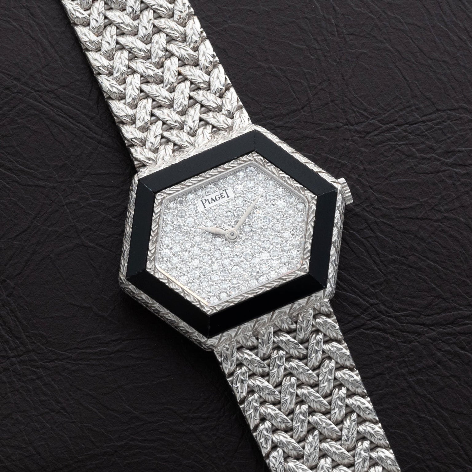 The Piaget Hexagonal Diamond Dress Watch features a woven silver band and rests on a dark textured surface.