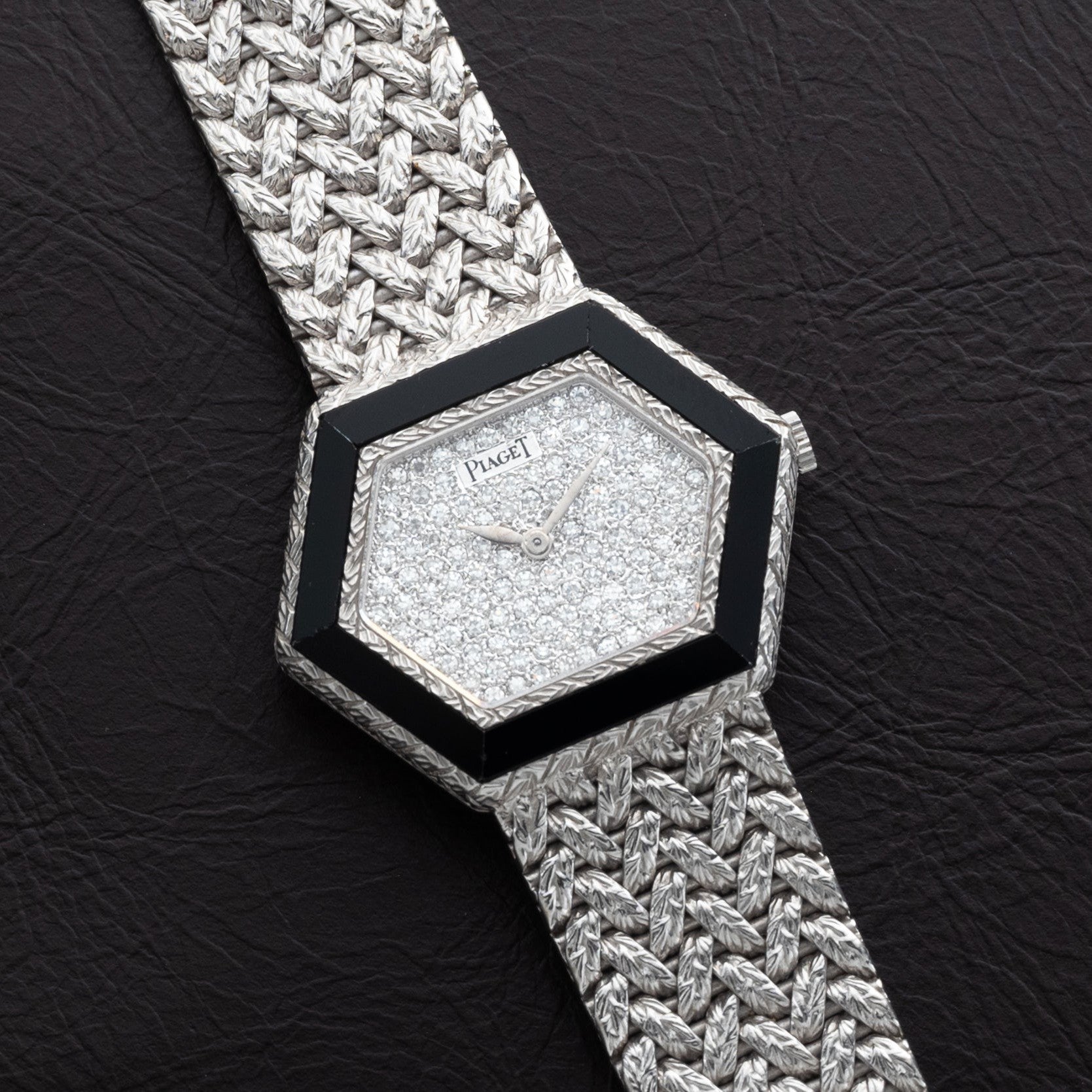 The Piaget Hexagonal Diamond Dress Watch features a woven silver band and rests on a dark textured surface.