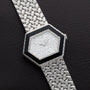 The Piaget Hexagonal Diamond Dress Watch features a woven silver band and rests on a dark textured surface.