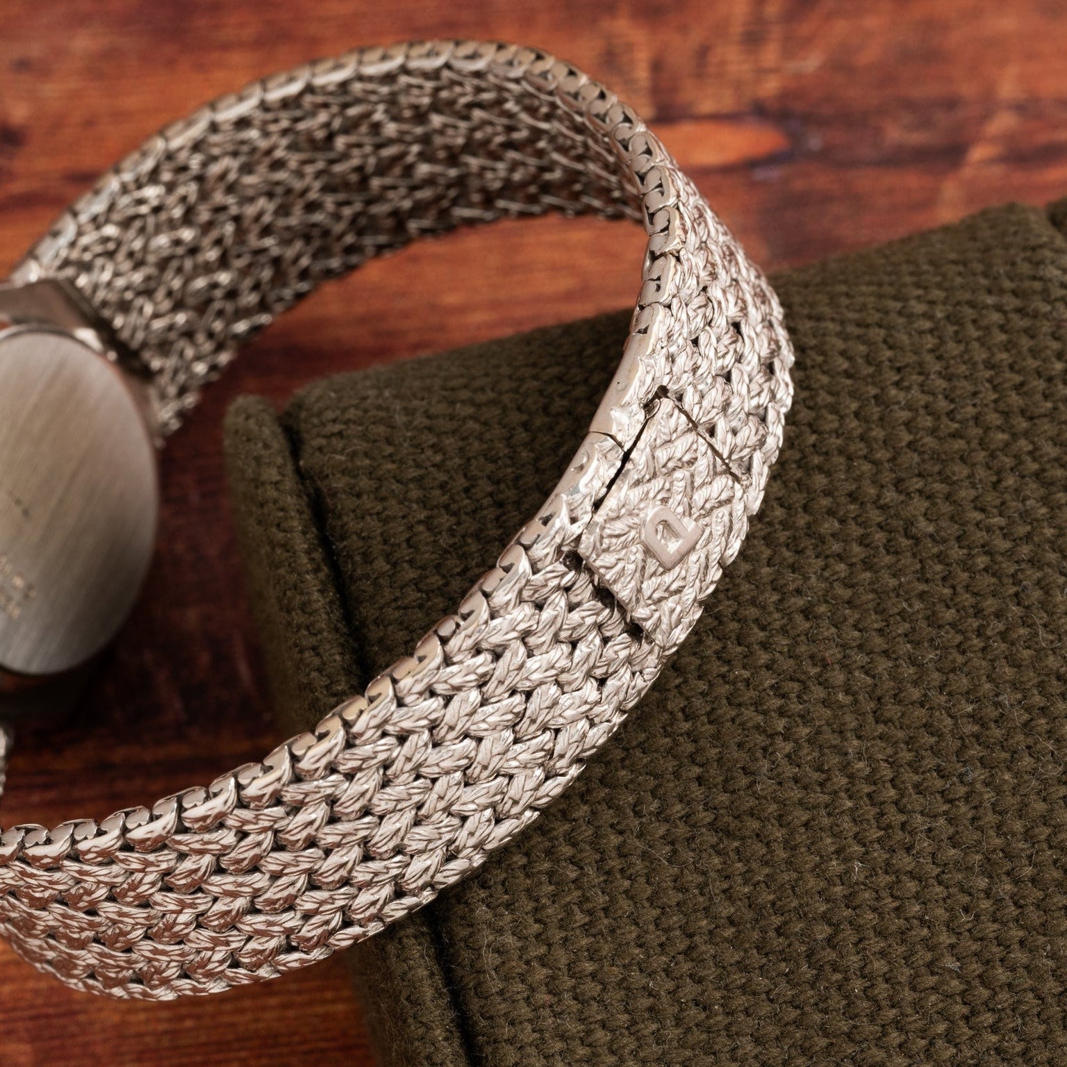 The Piaget Lapis Lazuli White Gold Dress Watch features a silver woven metal band with a clasp, displayed on a green textured surface.