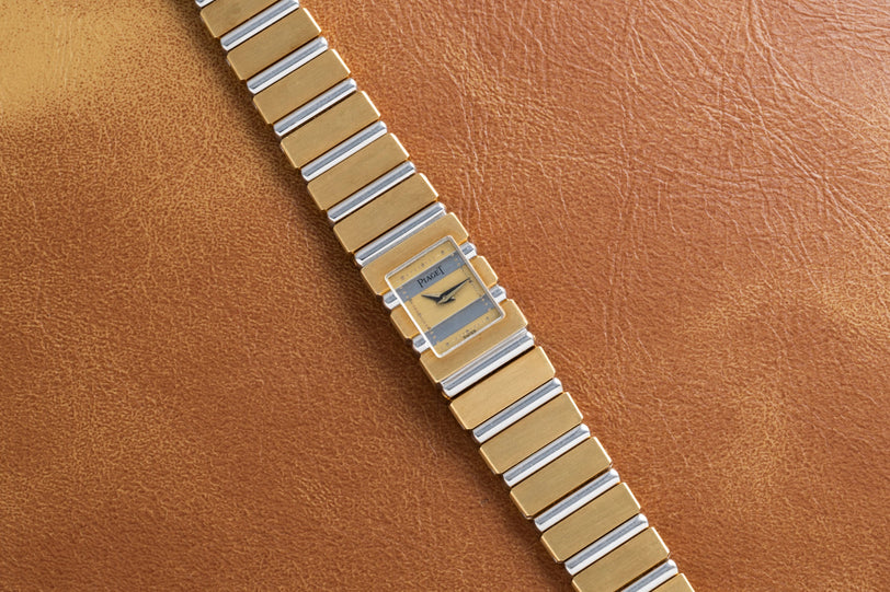 The Piaget Polo Square, a gold and silver wristwatch with a square face, rests on a brown leather surface.