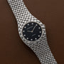 The Audemars Piguet Cobra is a silver watch featuring a black dial with diamond hour markers, displayed on a brown leather surface.