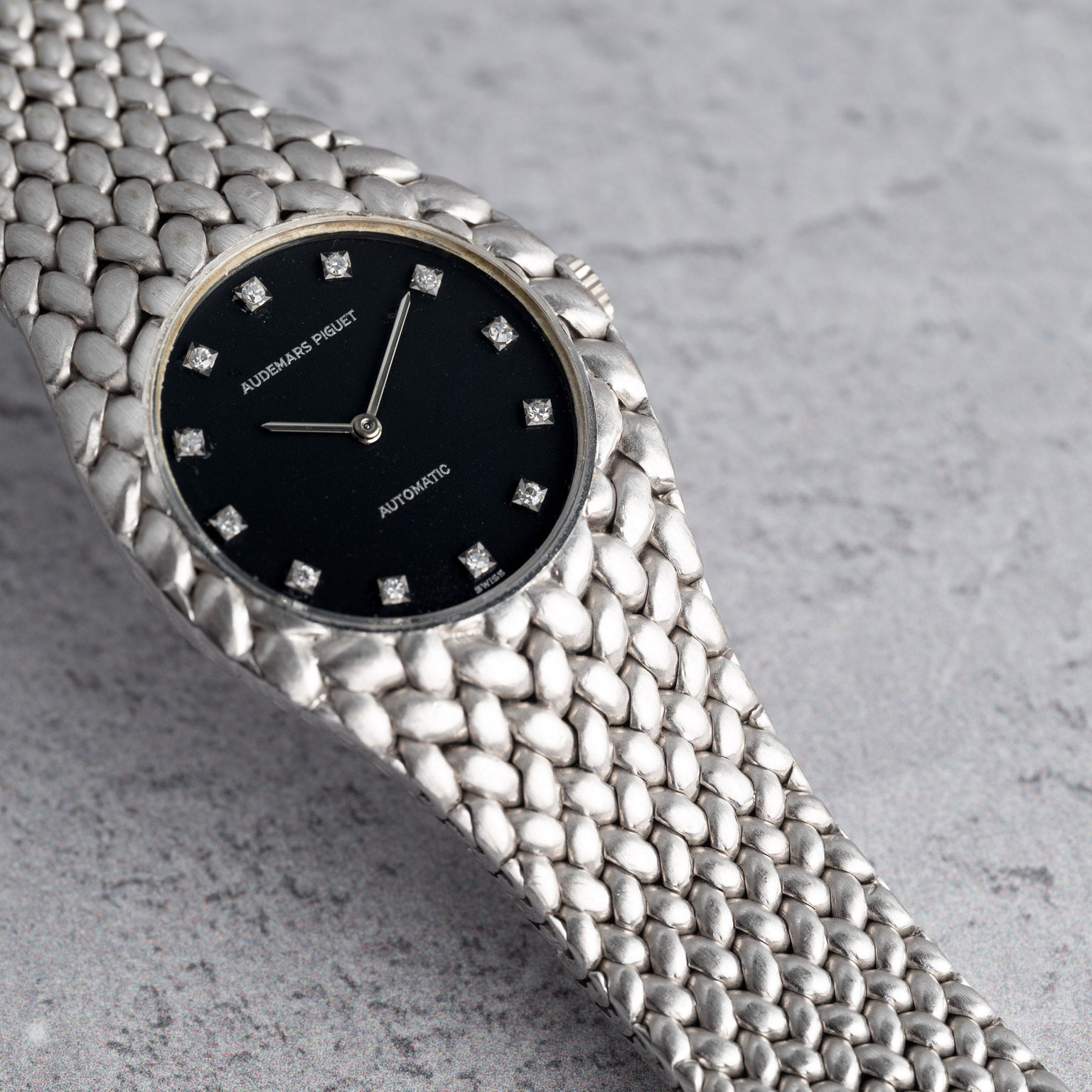 The Audemars Piguet Cobra is a luxury silver watch featuring a black dial, diamond hour markers, and a textured band.