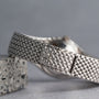 A close-up of the Audemars Piguet Cobra silver woven watch band resting on a speckled stone surface.