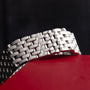 A close-up of the Cartier Panthère Ruban Mother Of Pearl silver metal watch band against a black and red background.