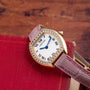 A Cartier Tortue gold watch with a pink strap and diamond bezel rests on a red book.