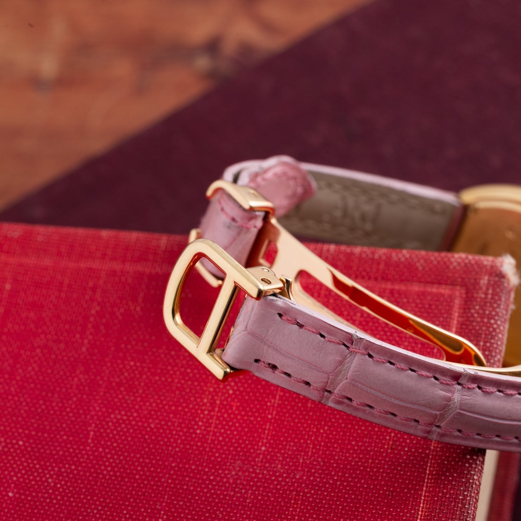 Close-up of a Cartier Tortue pink leather watch strap with a gold buckle, resting on a red textured book.